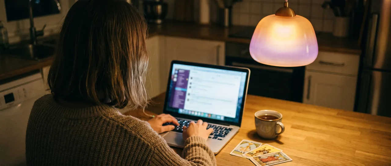 Kobieta pisze na czacie z wróżką przy laptopie, obok karty tarota